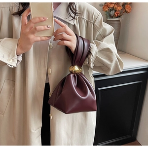 Detail of burgundy ruched cloud bag featuring luxury gold spherical metal knot handle