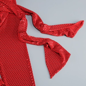 Détail du tissu rouge avec pois en paillettes noires et texture plissée sur la robe longue