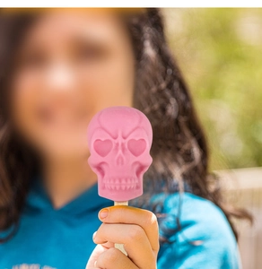 Glace à l'eau rose en forme de crâne avec yeux en cœur tenue à la main en plein air