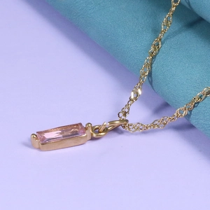 Detail of a pink rectangular zircon pendant on a gold necklace over a silk background