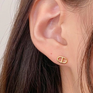 Detail shot of a minimalist gold-plated oval D-shape stud earring worn on the earlobe