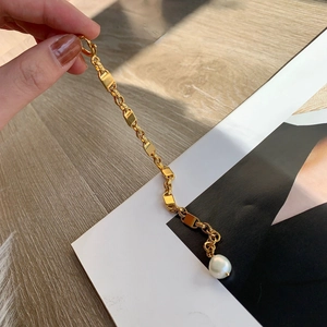 Bracelet chaîne plaqué or 18k avec pendentif perle carrée sur fond en bois naturel