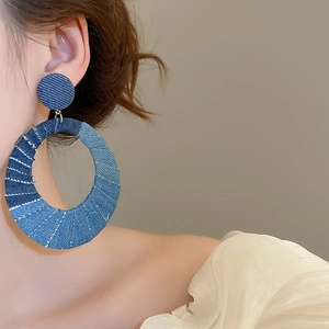 Detail of large oval denim fabric patchwork earrings worn by a female model