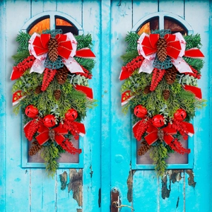 Christmas teardrop wreath with red bow, pine cones and bells hanging on a door