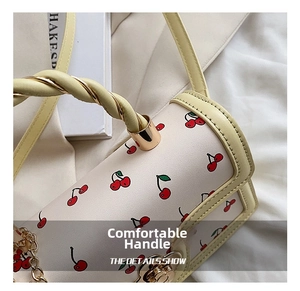 Detail of woven rope handle and gold hardware on cream crossbody bag with cherry prints