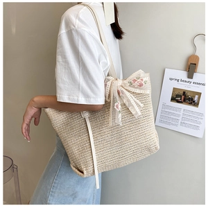Detail of straw tote bag with lace bow, floral embroidery and white leather strap