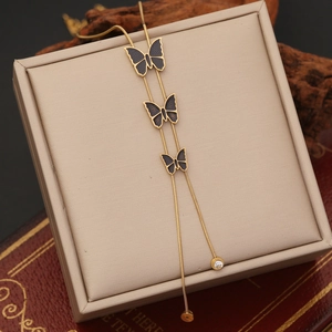 Elegant gold butterfly tassel necklace with black charms on a minimalist jewelry box