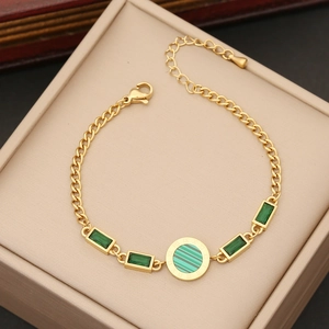 Gold chain bracelet with emerald green stones and roman numeral dial on velvet pad