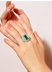 Close-up of emerald-cut green gemstone ring with pavé diamond halo on model's hand