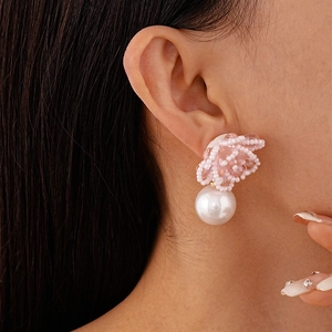 Close-up of pink beaded flower earrings with a large white faux pearl drop on a model