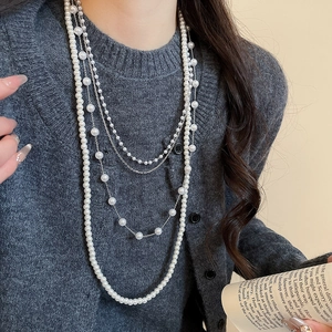 Detail of layered white faux pearls and silver metal chain necklace on a model
