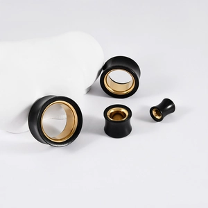 Macro detail of black and gold stainless steel ear gauges on white display stand