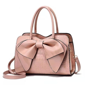 Detail view of pink bow handbag with crocodile pattern texture and golden hardware