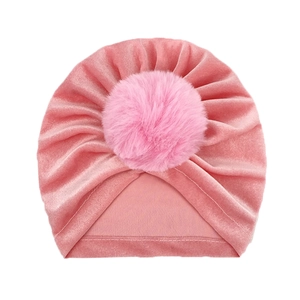 Pink velvet baby turban hat with soft faux fur pom pom decoration on white background