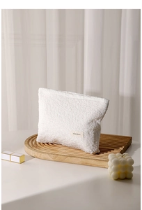 Detail view of white pleated lace cosmetic bag texture and brand label on a tray