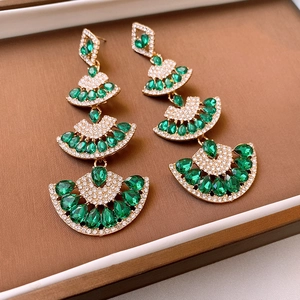 Detailed close-up of gold fan-shaped earrings with emerald stones and rhinestones
