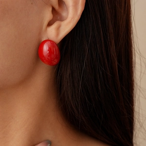 Close-up of a glossy red oval stud earring worn by a model for a vintage minimalist look