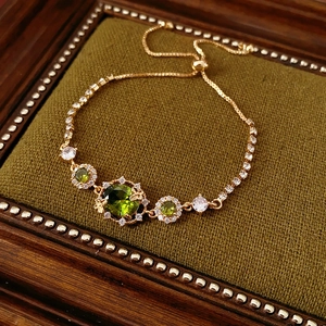 Détail d'un bracelet doré ajustable avec des pierres précieuses vertes et zircones