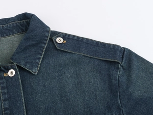 Détail du col d'une veste en jean bleu foncé avec coutures contrastées et boutons argentés
