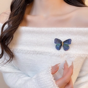 Detailed close-up of blue embroidery butterfly brooch on a white sweater