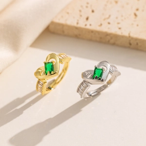Golden and silver heart rings with green rectangular gemstones on textured stone and fabric