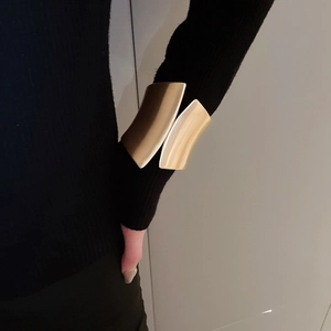 Close-up of wide gold irregular metal cuff bracelet worn over a sleek black sleeve