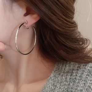 Close-up of a large polished silver round hoop earring worn by a model in warm light