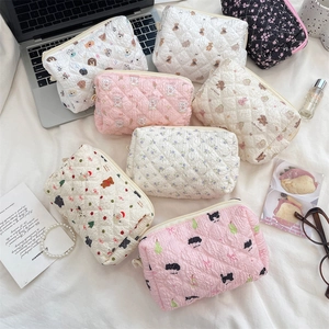 Quilted cosmetic bags with floral and animal prints arranged on a bed with a laptop