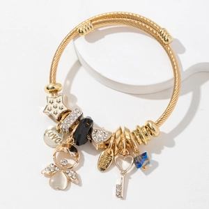 Golden mesh charm bracelet with angel, star and heart key pendants on white pedestal