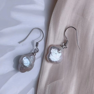 Detailed macro view of irregular baroque pearl earrings with silver ear hooks on satin