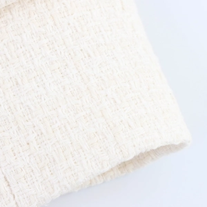 Close-up detail of cream white bouclé tweed fabric texture with intricate weaving patterns