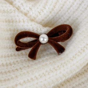 Close-up of a brown velvet bow hair clip with a center white pearl on beige knit