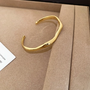 Detailed view of 18k gold plated wavy open bangle with polished mirror finish on jewelry tray