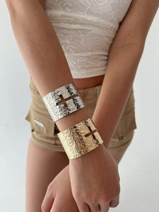 Detail of hammered metal open cuff bracelet featuring a religious cross cutout design