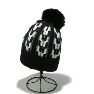 Detailed close-up of thick knit pom-pom hat with black and white jacquard pattern
