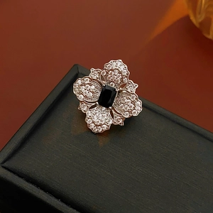 Macro detail of rose gold flower ring with black gemstone on textured jewelry box