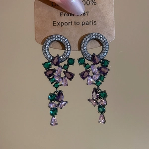 Detail view of ornate tassel earrings with purple and green crystals on silver needle studs