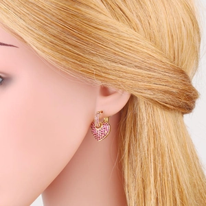Macro detail of gold heart earrings with pavé-set pink cubic zirconia on a model