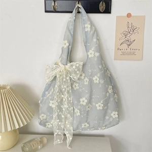 Detail of light blue embroidered tote bag with large lace bow on a wall hanger