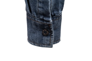 Close-up of blue denim shirt cuff with orange stitching and branded metal button detail