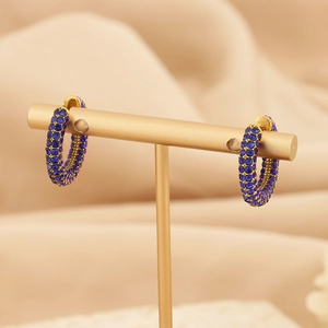 Close-up of gold-plated C-shaped earrings with micro-paved blue crystals on display