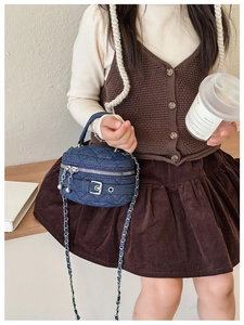 Detail of dark blue denim quilted mini bucket bag with silver chain strap and top handle