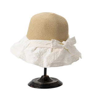 Women's wide brim straw sun hat with white fabric trim and a large bow on metal stand