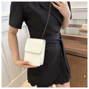 Close-up of a white mini flap bag with metal chain strap on a black dress outfit