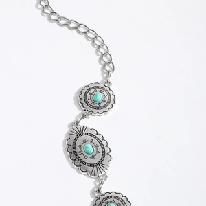 Close-up of engraved silver metal waist chain featuring oval turquoise gemstones