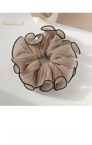 Close-up of beige pleated chiffon scrunchie with delicate black trim on white surface