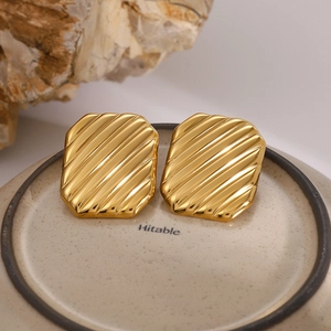 Macro shot of 18K gold plated square earrings with diagonal wave texture on ceramic tray
