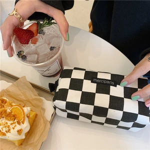 Detail of checkered canvas stationery bag with merciparis tag on a minimalist cafe table