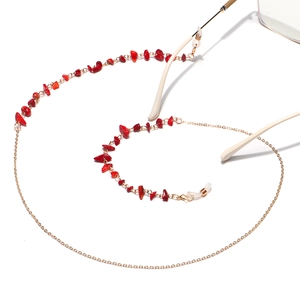 Detail of gold chain glasses strap featuring irregular red natural stone accents