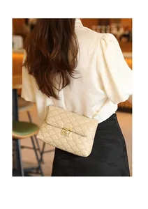 Détail d'un sac à main matelassé beige avec chaîne dorée porté par un mannequin
